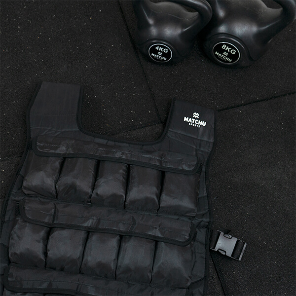 Gilet lesté noir Matchu Sports de 20 kg sur un sol de gymnase, avec des kettlebells en arrière-plan.